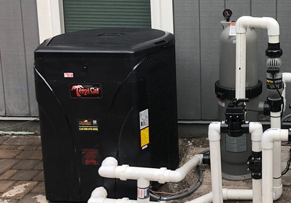A close-up of a black pool heater with white PVC plumbing connections.