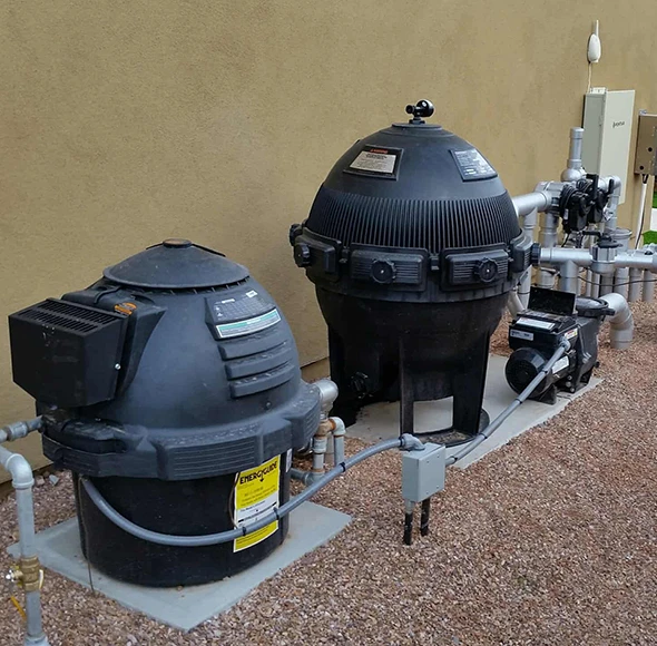 Two large, black pool filter tanks and a pump on a concrete pad.