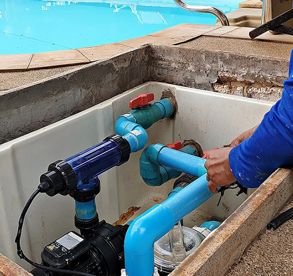 A pool technician installing blue PVC pipes for a pool pump and filter system.