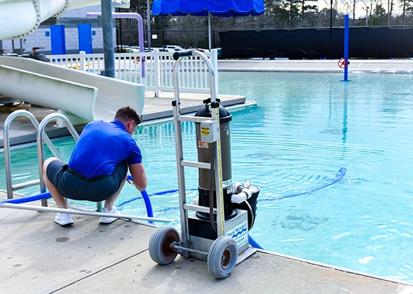 A pool technician using a robotic pool cleaner in a large swimming pool.