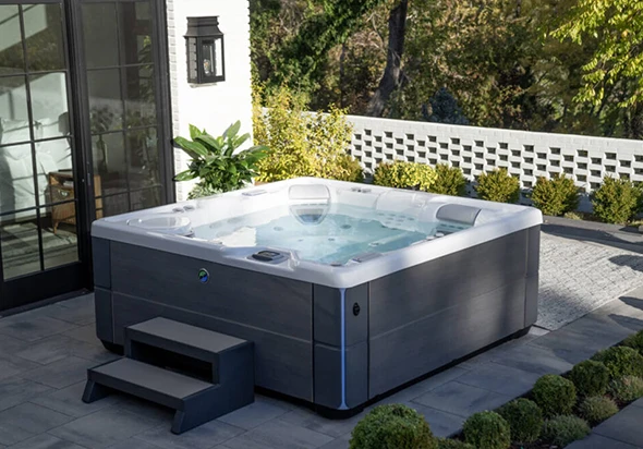 A large, modern hot tub on a patio with a stone wall and landscaping.