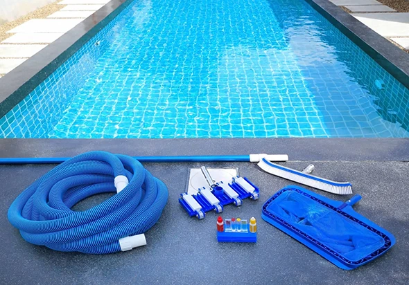 Pool cleaning equipment, including a hose, skimmer net, and brushes, next to a swimming pool.