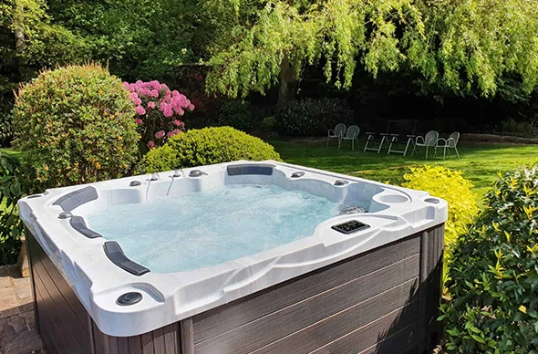 A hot tub in a backyard setting with trees and plants in the background.