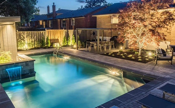 A luxurious swimming pool and spa at night, illuminated by underwater lights and surrounding landscape lighting.