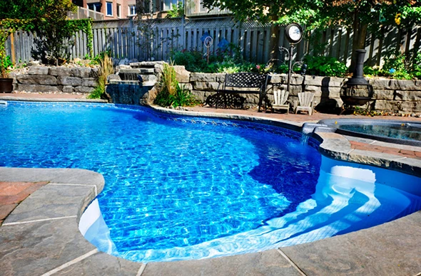 A view of a residential swimming pool with steps and a rock feature.