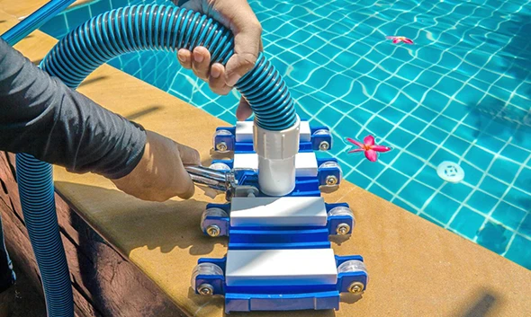 A pool pump connected to a blue hose, next to a swimming pool.