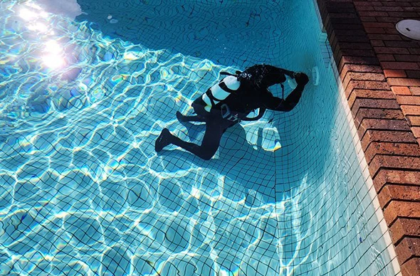 A person in scuba gear inspecting the bottom of a swimming pool.
