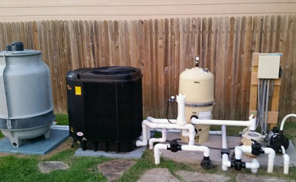A black pool heater and white filter system located in a backyard with a wooden fence.