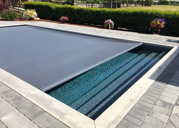 A swimming pool with a gray automatic pool cover partially rolled up.